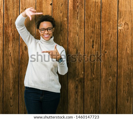 Young beautiful african american woman wearing glasses over isolated background smiling making frame with hands and fingers with happy face. Creativity and photography concept.