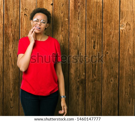 Beautiful young african american woman wearing glasses over isolated background touching mouth with hand with painful expression because of toothache or dental illness on teeth. Dentist concept.