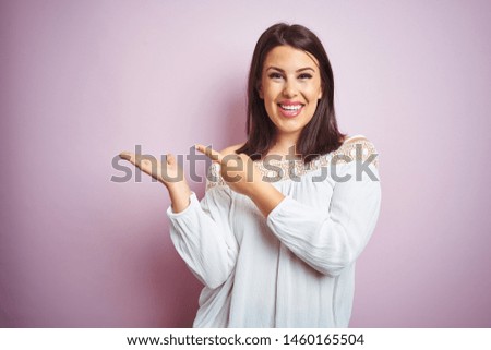 Young beautiful brunette woman over pink isolated background amazed and smiling to the camera while presenting with hand and pointing with finger.