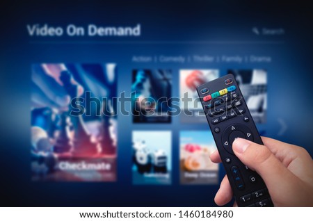 VOD service screen with remote control in hand. Video On Demand television internet stream multimedia concept Royalty-Free Stock Photo #1460184980