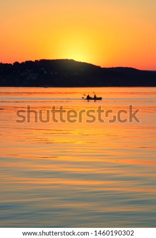 Magical golden orange  sunset on the Lake Balaton with people canoe man on water and behind them is the mountains.