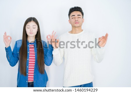 Beautiful young asian couple over white isolated background relax and smiling with eyes closed doing meditation gesture with fingers. Yoga concept.