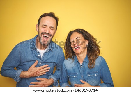 Beautiful middle age couple together standing over isolated yellow background smiling and laughing hard out loud because funny crazy joke with hands on body. Royalty-Free Stock Photo #1460198714