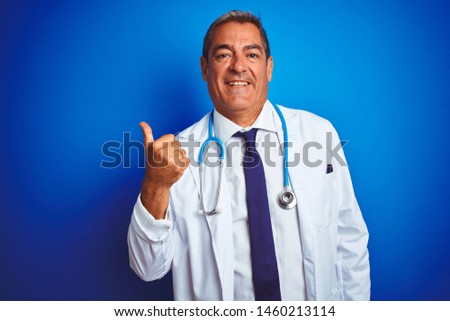 Handsome middle age doctor man wearing stethoscope over isolated blue background doing happy thumbs up gesture with hand. Approving expression looking at the camera showing success.