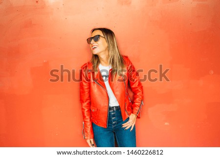 Happy young woman with sunglasses and red leather jacket on red background.
