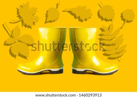 autumn composition of yellow rubber boots and leaves on a yellow background