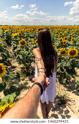 Beautiful brunett girl in white dress hand in hand going to sunflowers field.