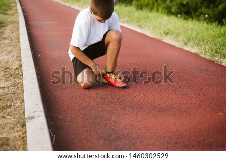 The little boy athlete ties his shoelaces and prepares for training on the athletic track