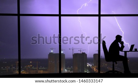 The man working at the table near a window on a city lightning background