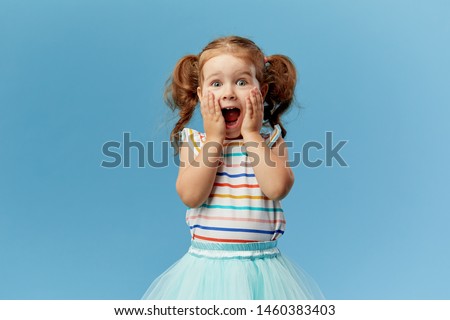Portrait of surprised cute little toddler girl child standing isolated over blue background. Looking at camera. hands near open mouth Royalty-Free Stock Photo #1460383403