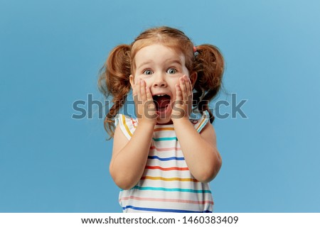 Portrait of surprised cute little toddler girl child standing isolated over blue background. Looking at camera. hands near open mouth Royalty-Free Stock Photo #1460383409
