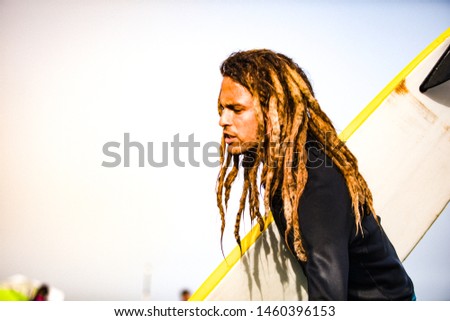 Lifestyle photography. A day in summer of a surf coach in a sunny beach.
 Young man with dreadlocks outdoors. 