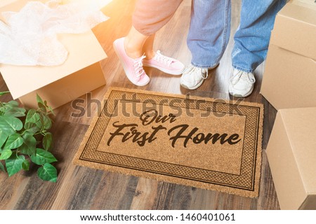 Man and Woman Unpacking Near Our First Home Welcome Mat, Moving Boxes and Plant. Royalty-Free Stock Photo #1460401061