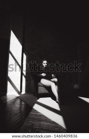 Beautiful pregnant woman sits on the chair in front of big window. Black and white photo