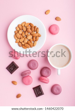 Purple and pink macaron or macaroon cakes with cup of coffee and almonds on pastel pink background. Morninig, spring, fashion composition. Flat lay, top view, pattern.