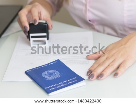 A portfolio of Brazilian workers (Translation "Work Permit, Ministry of Labor and Social Security Brazil CTPS"), female hand stamping a work contract background