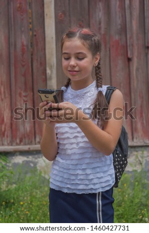 close up portrait of little beautiful stylish kid girl near red wall as background. White blouse, blue skirt - school clothes. Soon to school. Modern. Two pigtails in a child. The girl with the phone.