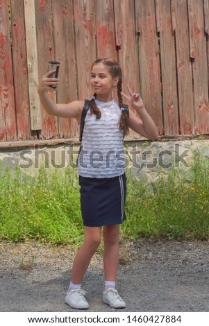 close up portrait of little beautiful stylish kid girl near red wall as background. White blouse, blue skirt - school clothes. Soon to school. Modern. Two pigtails in a child. The girl with the phone.
