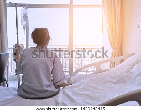 Asian women are sick and are hospitalized. The patient is sitting in the bed waiting to receive treatment from the doctor in the room.