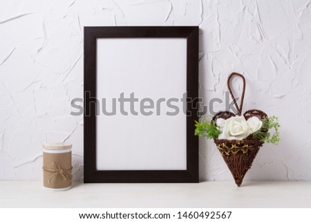 Black brown  frame mockup with white roses in the wicker heart flower pot. Empty frame mock up for presentation design. Template framing for modern art.