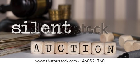 Words SILENT AUCTION composed of wooden dices. Auction gavel on the table in the background. Closeup Royalty-Free Stock Photo #1460521760
