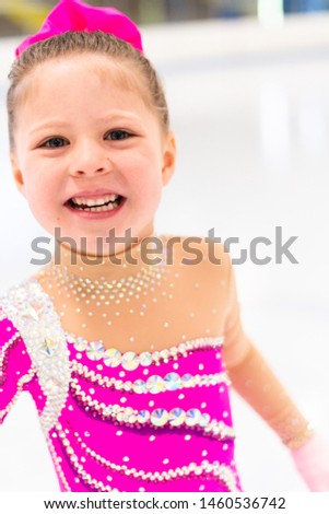 Little figure skater in pink dress practicing on the indoor ice rink.