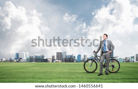 Pleasant man in business suit and tie standing on green grass with bike. Be active concept. Cheerful businessman with bicycle relax on green meadow at sunny day. Happy and successful business people