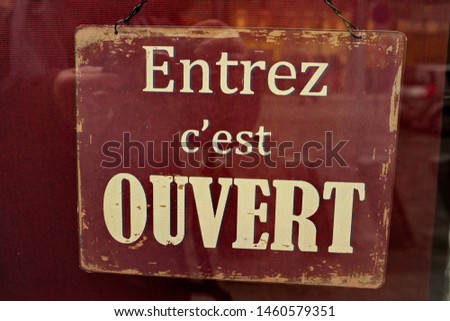 French text: Entrez, c'est ouvert. 
English translation:  Enter, it's open. Panel behind a glass door store.