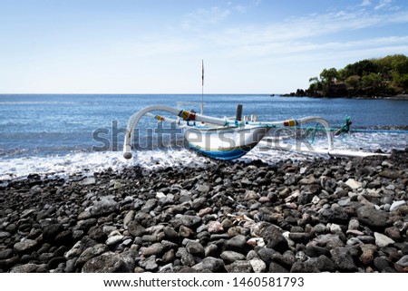A fishing boat shored on the beach of Tulamben, Bali with blue skies in background and calm sea.