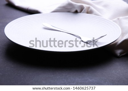 Clean white plate, fork and napkin on black background. Concept table setting.