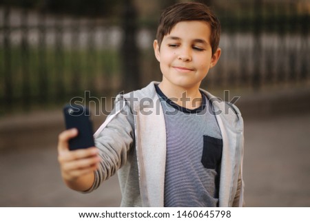 Young boy make a selfie on smartphone in the centre of the city. Cute boy in blue hat. Stylish school boy