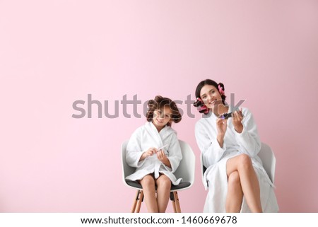 Mother and her little daughter in bathrobes manicuring nails against color background