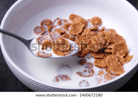 Crispy healthy dry cereal with milk in deep plate with spoon on black background.