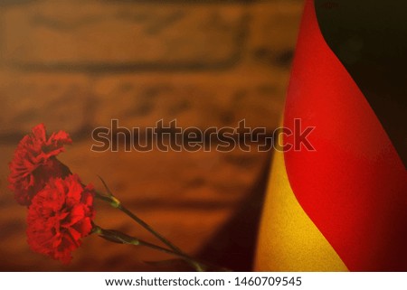 Germany flag with two red carnation flowers for honour of veterans or memorial day on orange blurred painted brick wall mockup. Germany glory to the heroes of war concept.