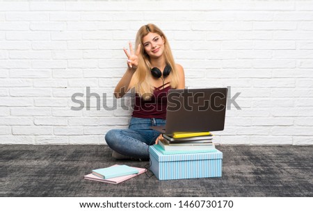Teenager girl sitting on the floor with her laptop happy and counting three with fingers
