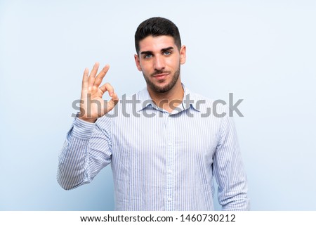 Caucasian handsome man over isolated blue background showing an ok sign with fingers