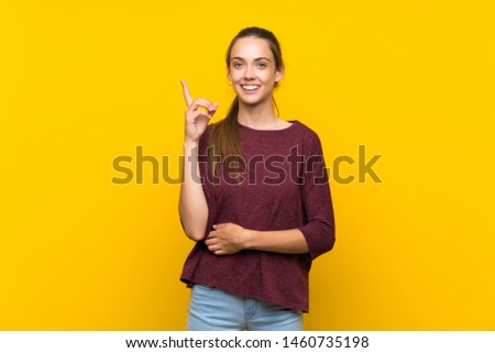 Young woman over isolated yellow background showing and lifting a finger in sign of the best