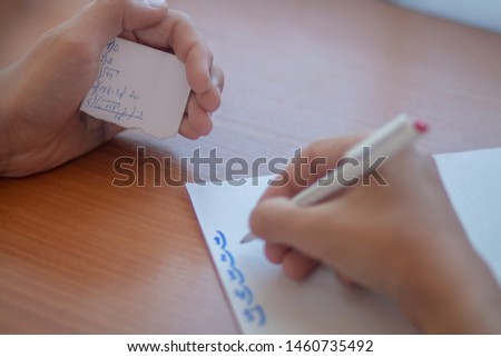 Teenager cheating in test exam with answer piece of paper in school.