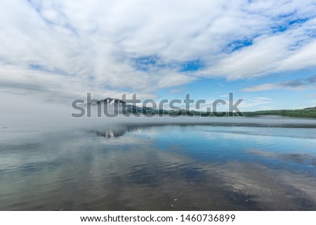 beautiful misty morning on Kurile lake in Kamchatka with active volcano and clouds