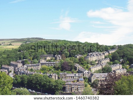 a scenic aerial view of the town of hebden bridge in west yorkshire with streets of stone houses and roads between trees and a blue summer cloudy sky Royalty-Free Stock Photo #1460740382