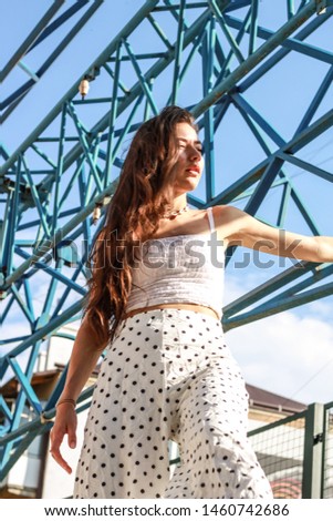 Portrait shooting of a stylish girl.Trends summer 2019.
White top, shirt, wide trousers.
Graffiti, blue arches and frames background. Fashion looks.Photo for brand advertising
