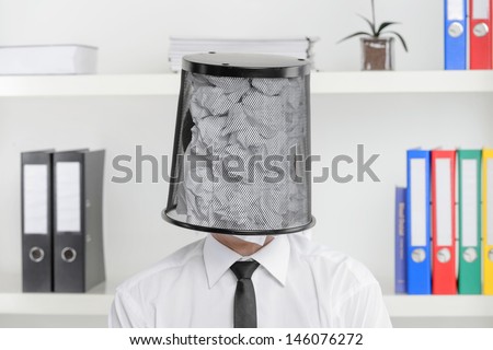 Tired of paperwork. Portrait of businessman sitting with a wastepaper basket on his head
