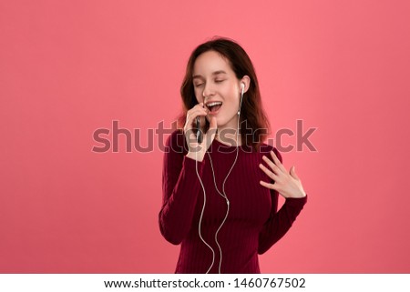 Happy young brunette woman singing and dancing using smartphone as a microphone and wearing wired headset.
