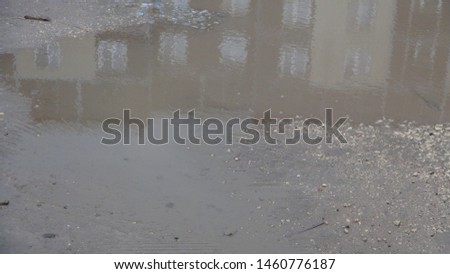 reflection of a multistory apartment building in a muddy and brown puddle