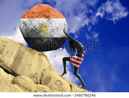 The girl wrapped in the flag of the United States of America, raises a stone to the top in the form of the silhouette of the flag of Egypt
