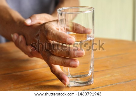 Elderly man is holding his hand while drinking water because Parkinson's disease.Tremor is most symptom and make a trouble for doing activities such as eat or drink.Health care or elderly concept. Royalty-Free Stock Photo #1460791943
