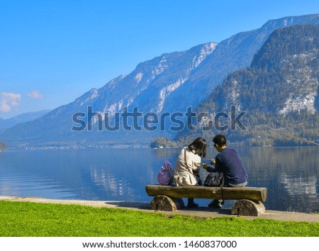 rear view of coule looking pictures on smartphone at the lake with green  yard and mountain