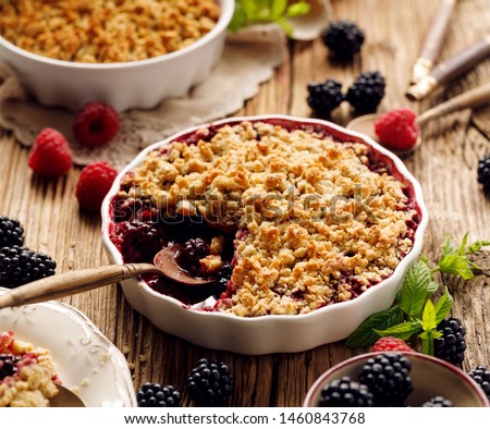 Crumble, Mixed berry (blackberry, raspberry) crumble, stewed fruits topped with crumble of oatmeal, almond flour, butter and sugar  in a baking dish on a wooden table, close-up Royalty-Free Stock Photo #1460843768