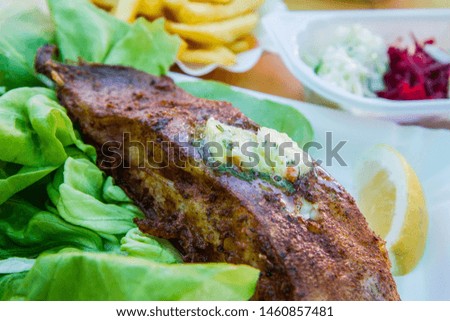 Fried halibut with garlic butter, lemon and lettuce with french fries and salad on the side on a paper tray