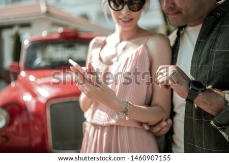 Sharing interests. Smiling woman showing her interested husband pictures on her smartphone standing with him in the street.
